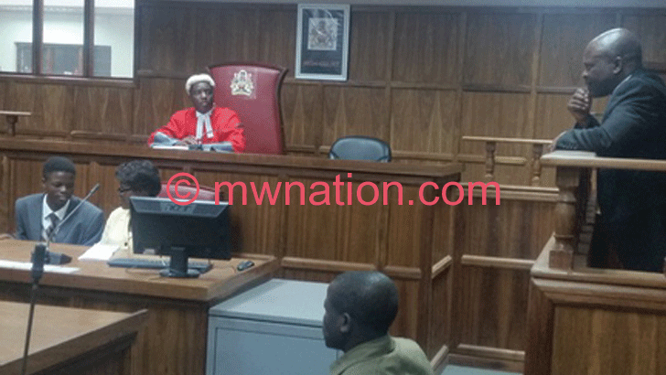 Manganya (R) stands in the dock as he listens to the judge