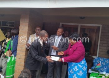 Chazama (R) gives out a cheque to one of the beneficiaries on behalf of Comsip